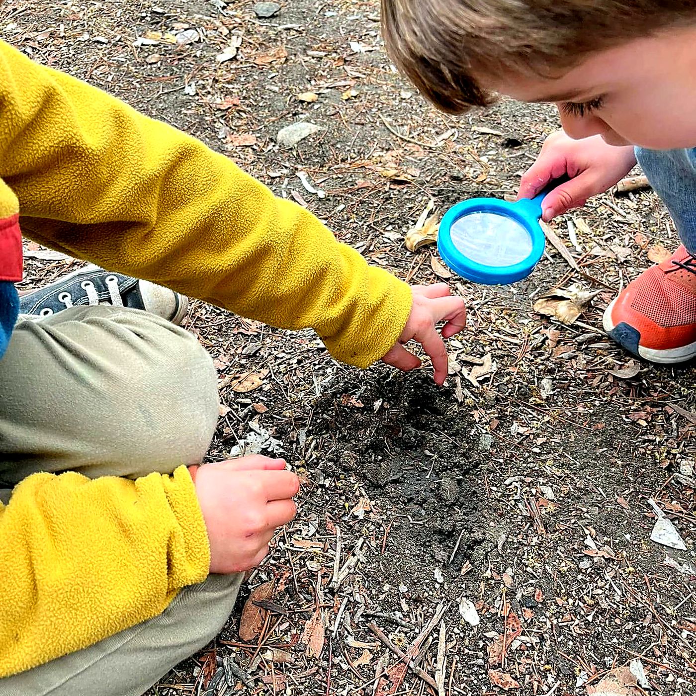 Two children digging in the soil with a magnifying glass